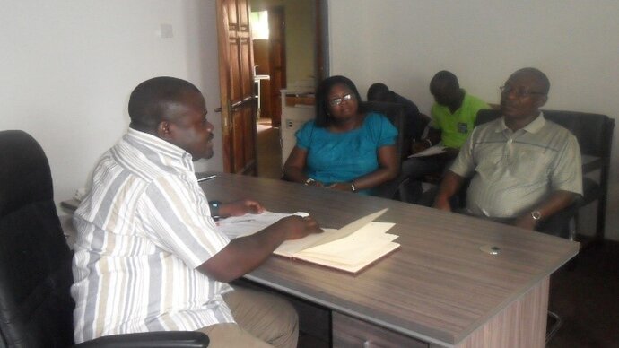 A woman and three men meeting around a desk in an office