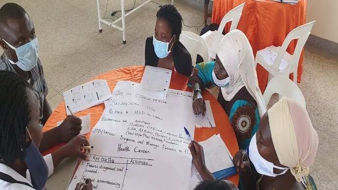 A group of masked African men and women discussing and writing on a piece of flipchart paper