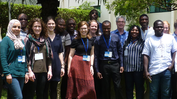 A row of seven standing, smiling African and European men and women in a garden