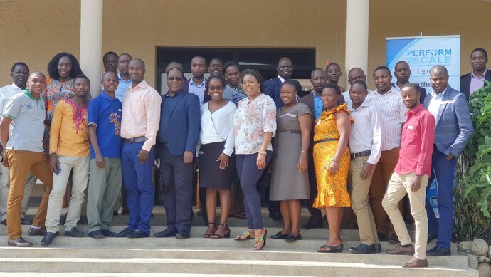 A group of standing, smiling African men and women pose of steps outside a building