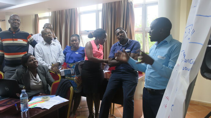 A group of African men and women standing around a flipchart while a man talks