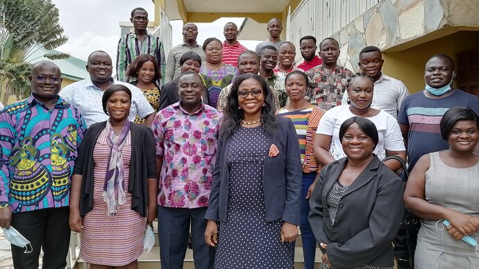 A group of smiling Ghanaian men and women standing on steps outside a building