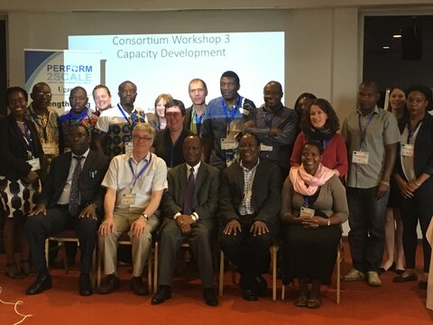 Dr Henry Mwebesa (centre front) and Dr Joseph Okware (front, far left) join consortium members at the PERFORM2Scale health systems strengthening workshop in Kampala. Rows and standing and seated smiling people