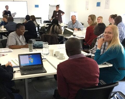 A seated women smiles at the camera while other Africa and European men and women sit around her