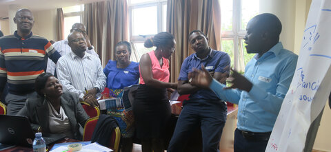 A group of African men and women standing around a flipchart while a man stands talking