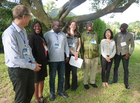 A group of seven standing, smiling African and European men and women in a garden