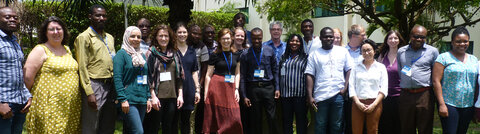 A large group of standing, smiling African and European men and women in a garden
